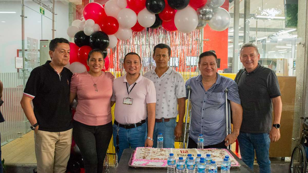 Una fotografía que muestra a un grupo de estudiantes y docentes de la Universidad Piloto de Colombia, Seccional del Alto Magdalena, durante la celebración del Día del Ingeniero 2024. De fondo se ven unos globos festivos y en la mesa que tienen en frente se observa una torta grande con el logo de la Universidad.