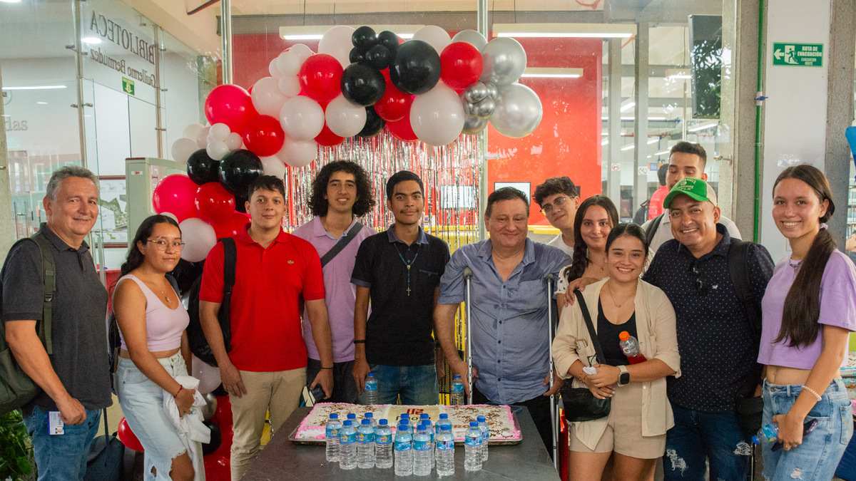 Una fotografía que muestra a un grupo de estudiantes y docentes de la Universidad Piloto de Colombia, Seccional del Alto Magdalena, durante la celebración del Día del Ingeniero 2024. De fondo se ven unos globos festivos y en la mesa que tienen en frente se observa una torta grande con el logo de la Universidad.