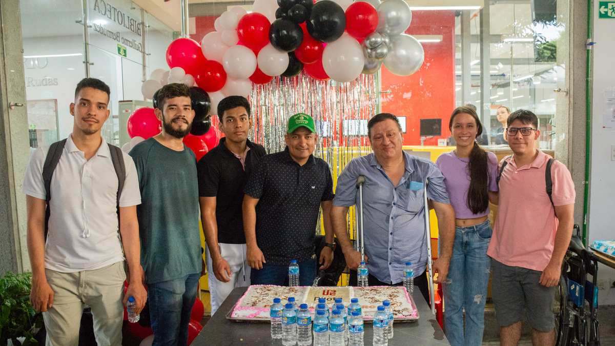 Una fotografía que muestra a un grupo de estudiantes y docentes de la Universidad Piloto de Colombia, Seccional del Alto Magdalena, durante la celebración del Día del Ingeniero 2024. De fondo se ven unos globos festivos y en la mesa que tienen en frente se observa una torta grande con el logo de la Universidad.