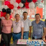 Una fotografía que muestra a un grupo de estudiantes y docentes de la Universidad Piloto de Colombia, Seccional del Alto Magdalena, durante la celebración del Día del Ingeniero 2024. De fondo se ven unos globos festivos y en la mesa que tienen en frente se observa una torta grande con el logo de la Universidad.