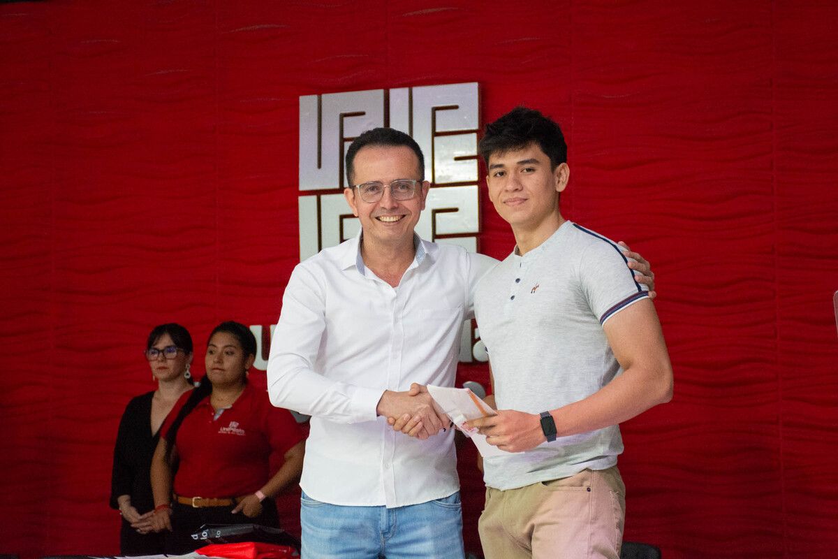 Una foto que muestra al docente de la UniPiloto en un apretón de manos con un estudiante, mientras le entrega el kit del Lápiz, durante la Ceremonia del Lápiz, en el Auditorio Principal de la Universidad Piloto de Colombia, Seccional del Alto Magdalena, en Girardot.