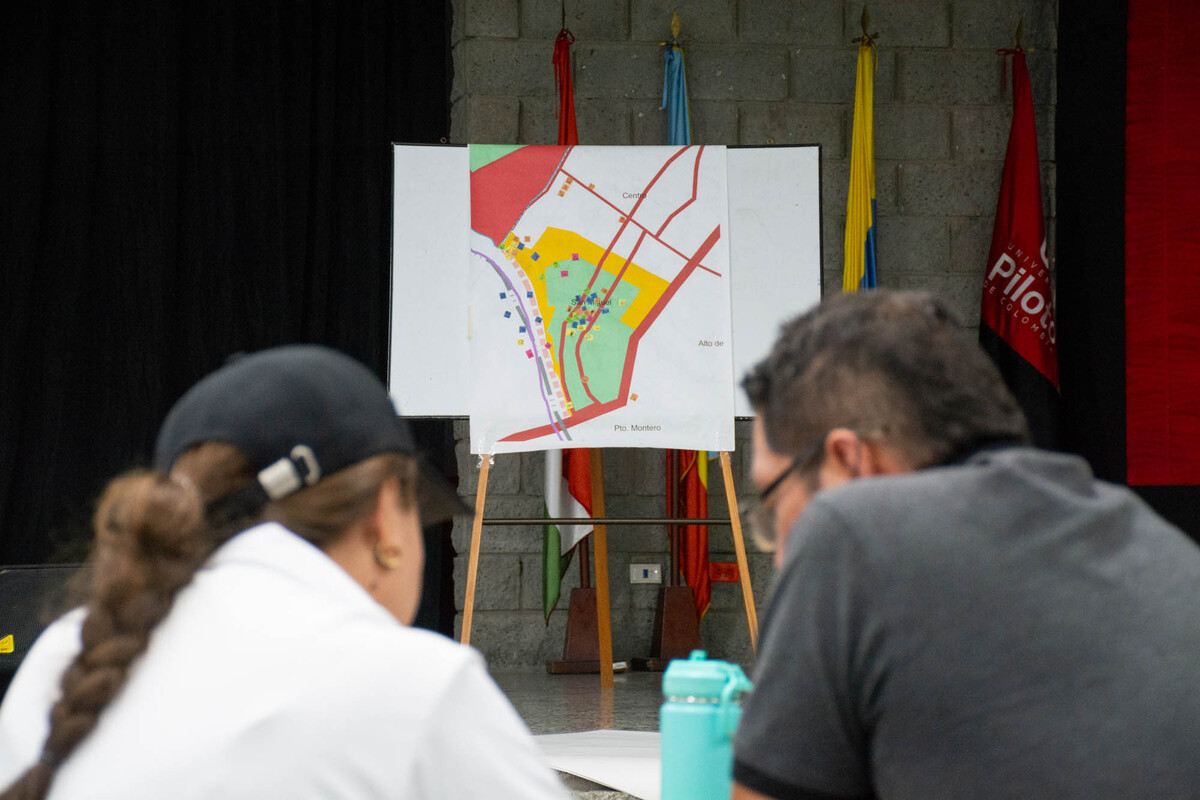 Dos participantes del tercer grupo focal de la Universidad Piloto de Colombia en Girardot, debaten propuestas de cartografía social para la Plaza de Mercado, con un mapa de fondo.