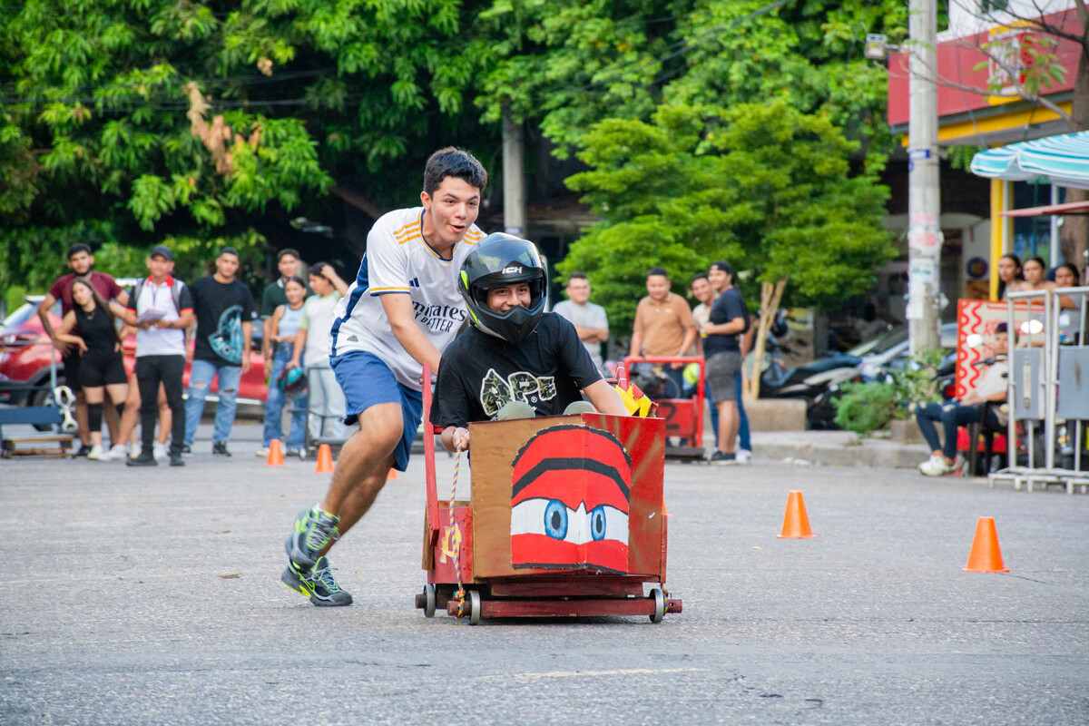 Un equipo participante corre con su carro de balineras mientras sus integrantes lo empujan con entusiasmo en plena competencia de la Semana Universitaria 2024.