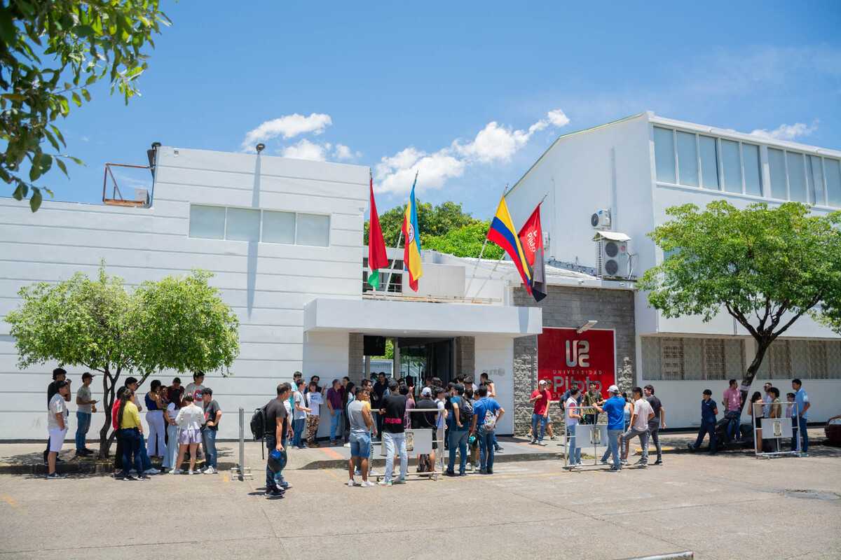 Una foto de la fachada principal de la Universidad Piloto de Colombia. Afuera se observan estudiantes participando en una capacitación para un simulacro de evacuación durante la Semana de la Salud 2024.