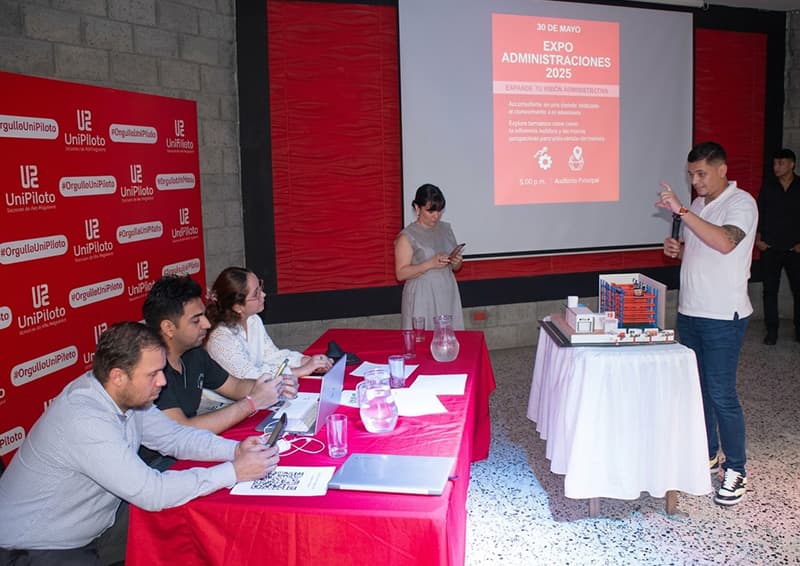 Estudiante exponiendo una maqueta técnica de logística frente a jurados evaluadores durante el evento ExpoAdministración 2025 de los programas de Administración Logística en la Universidad Piloto de Colombia